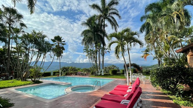 A pool area with red lounge chairs, a hot tub, and palm trees.