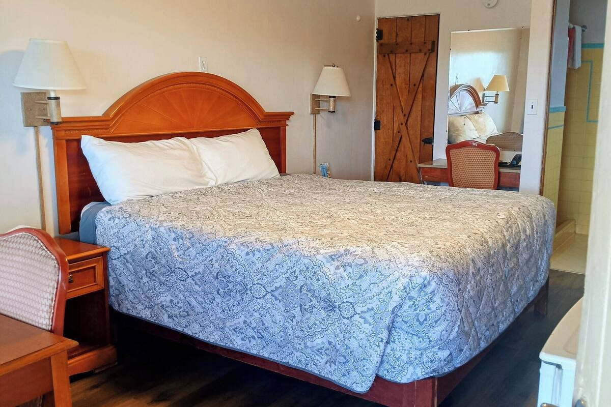 A bedroom with a wooden bed, two bedside lamps, a wooden nightstand, a chair, and a mirror.