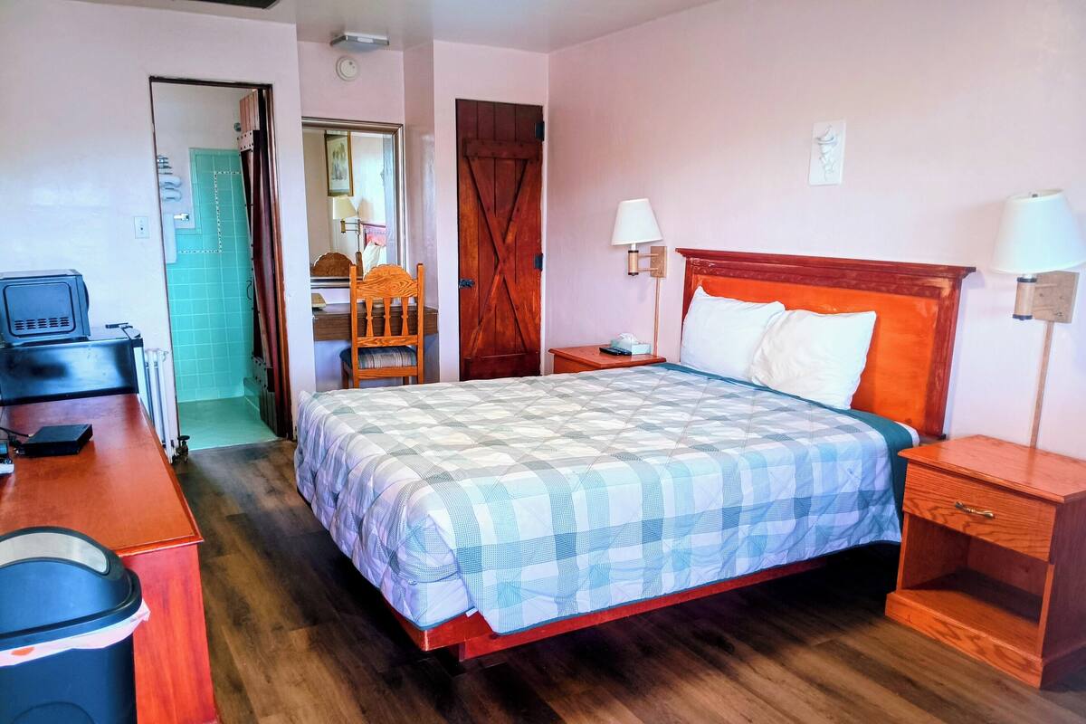 A bedroom with a wooden bed, a desk with a computer, a chair, and a wardrobe.