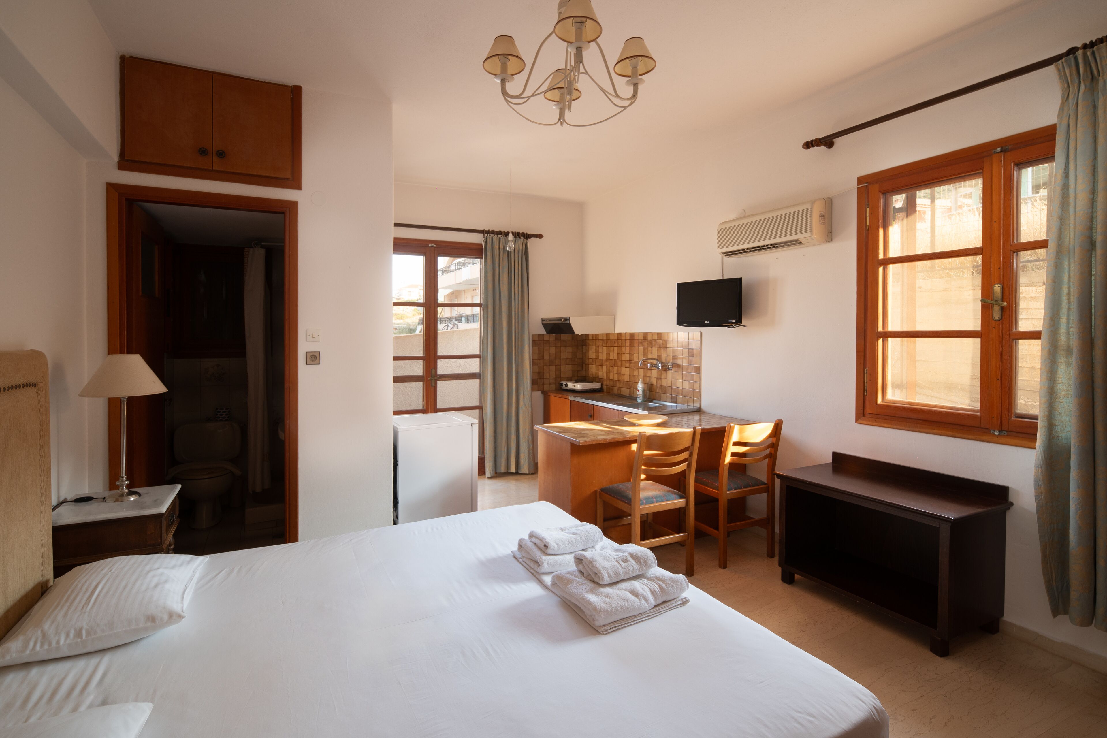 A hotel room with a large bed, a desk with a chair, a television, and a wardrobe.