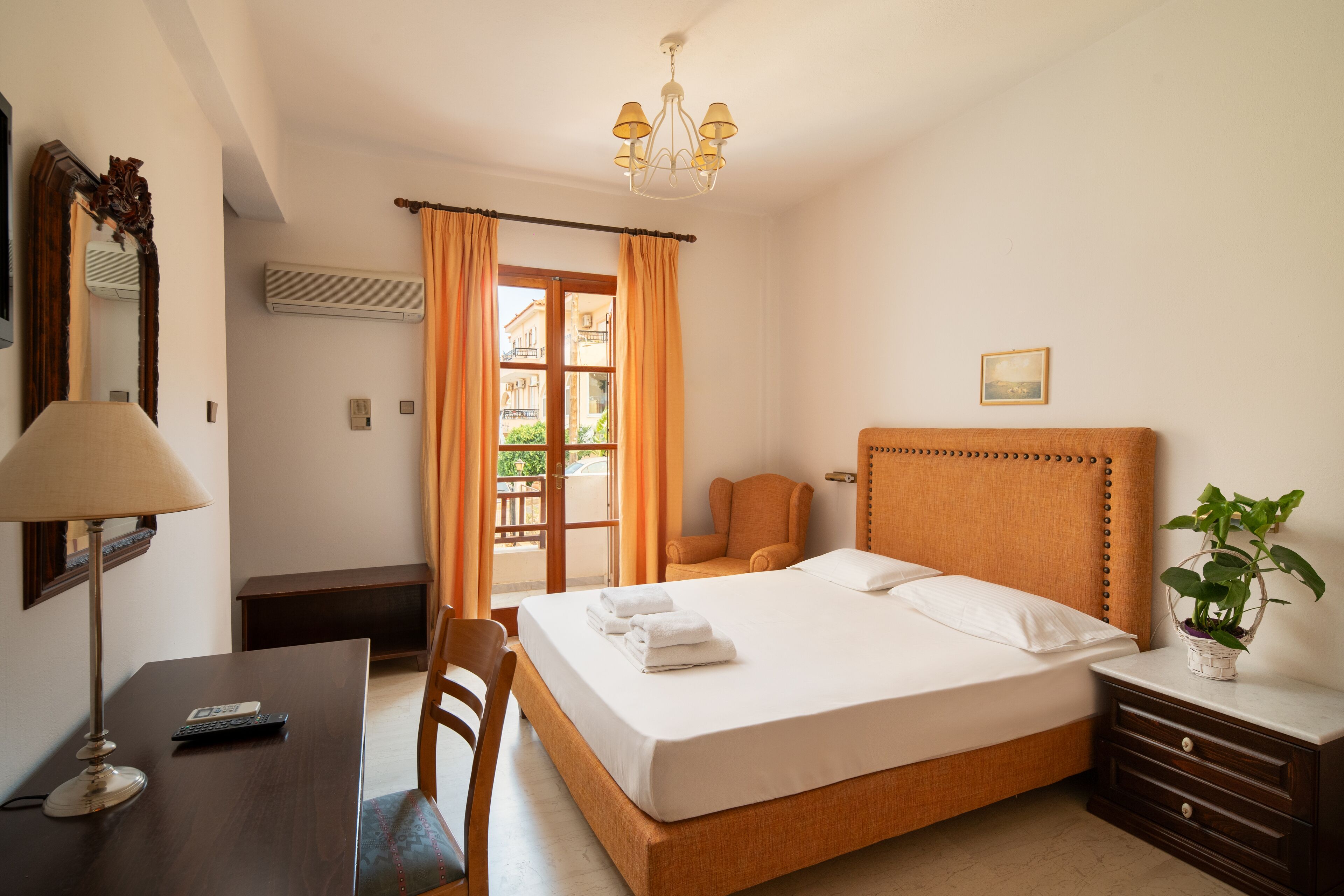 Una habitación de hotel con cama, mesita de noche, silla, escritorio, lámpara y una planta en maceta.