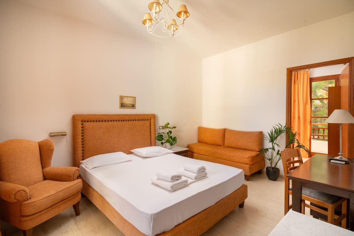 A hotel room with a large bed, a sofa, a dining table, and a chandelier.