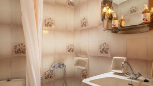 A bathroom with a toilet, shower, sink, and a mirror with a shelf above it. - Alta Vista Studios (Monemvasia)