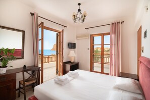 Habitación de hotel con cama, escritorio, silla, televisor y balcón con cortinas.