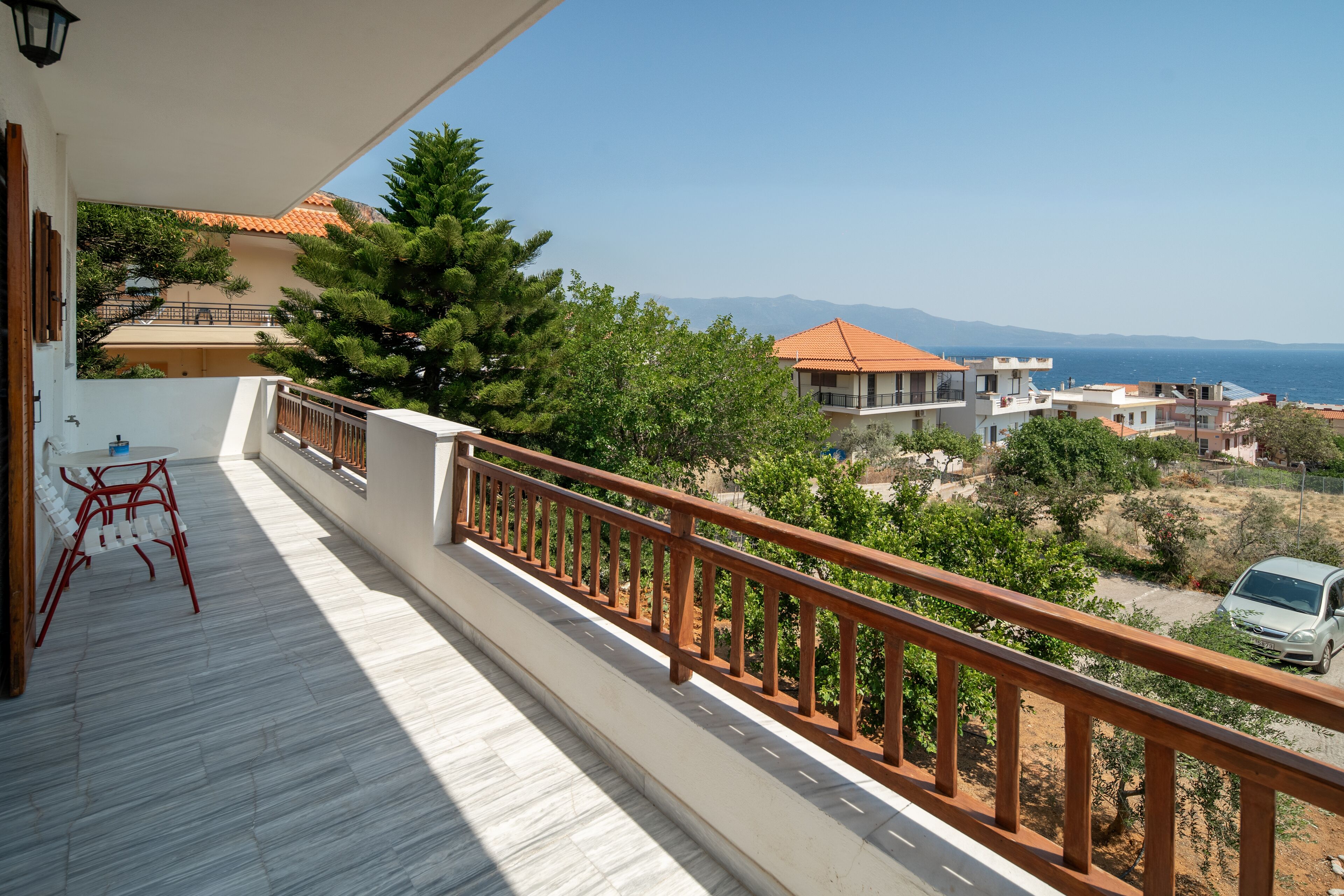 Varanda com grade de madeira, vista para área residencial com casas e mar aberto.