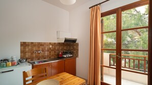 A kitchen with a wooden table and chairs, a tiled backsplash, and a window with curtains. - Alta Vista Studios (Monemvasia)