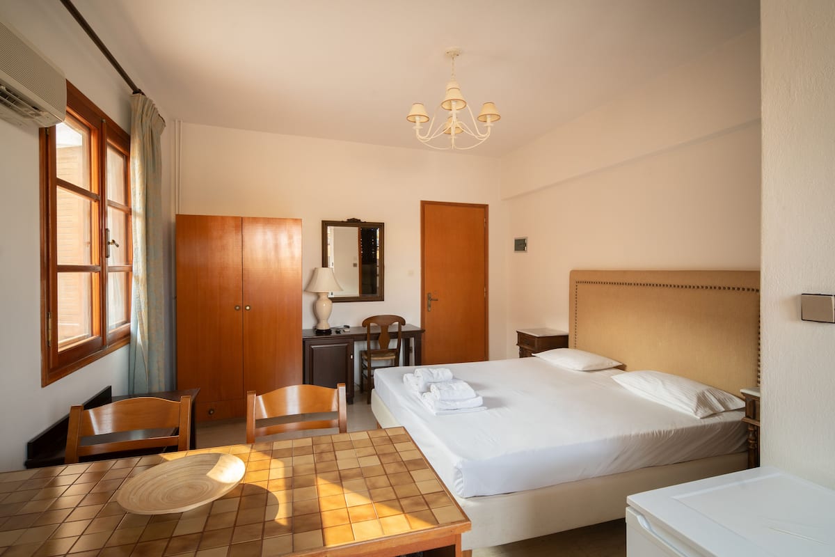 A hotel room with a bed, a desk, a chair, a table, a mirror, and a chandelier.