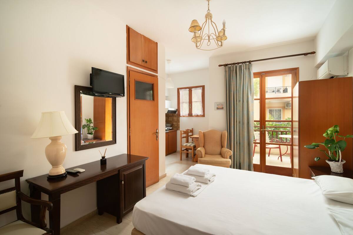 A hotel room with a bed, a desk, a TV, a chair, and a balcony.