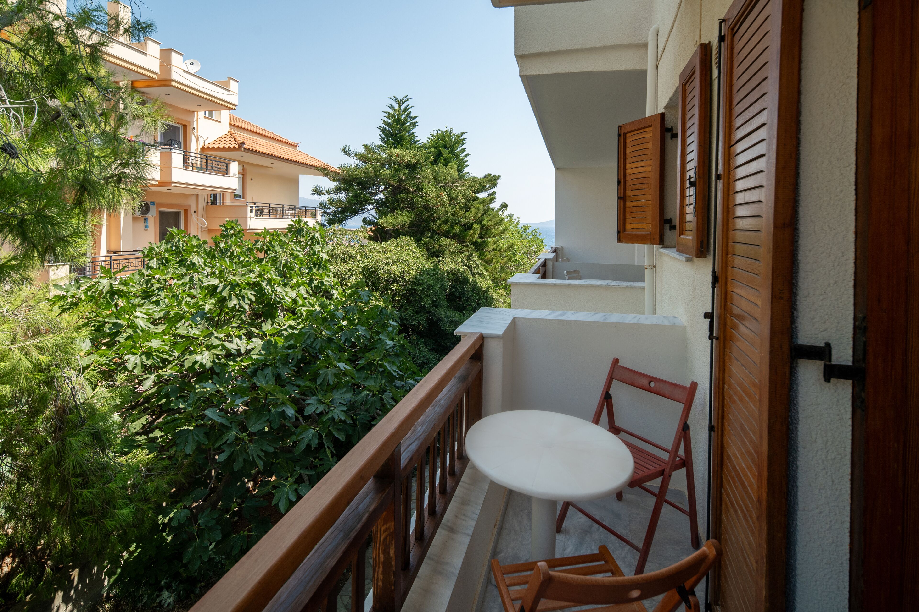 A balcony with a table and chairs, surrounded by greenery and adjacent buildings.