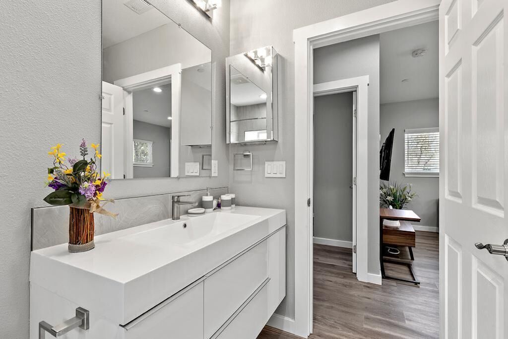 A modern bathroom with a large mirror, a white sink, and a vase of flowers.