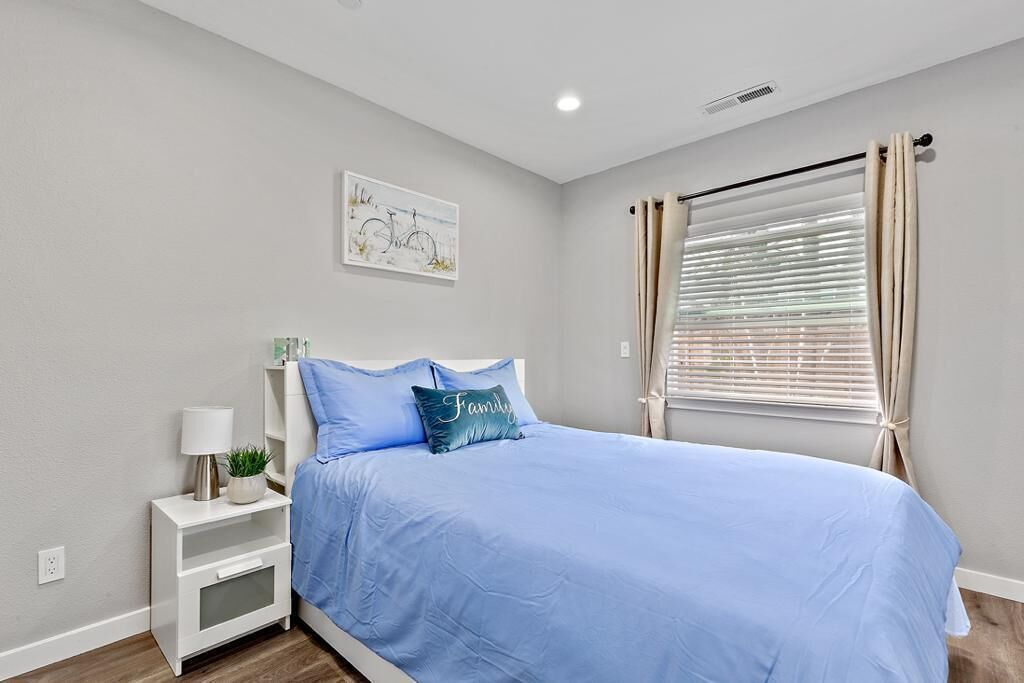 A bedroom with a bed, a nightstand, a lamp, a potted plant, and a window with curtains.
