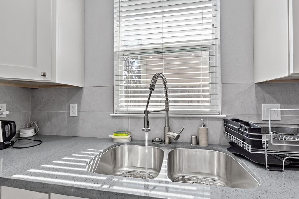 Una cocina moderna con un lavamanos de acero inoxidable doble, una tetera y un escurreplatos.