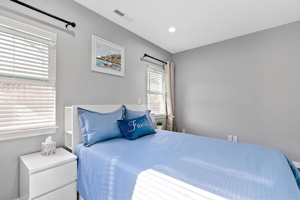 A bedroom with a large bed, white nightstands, and a window with blinds.