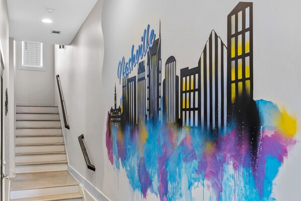 Una escalera conduce a una habitación con un mural vibrante de un paisaje urbano en la pared.