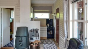 A compact kitchen with a stove, sink, and window. There is a small dining area with a chair and a table.