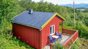 A red cabin with a black roof, a balcony with blue chairs, and a flagpole.