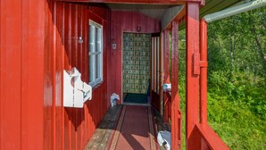 A red wooden building with a covered porch, a patterned rug, and a door with a green patterned curtain.