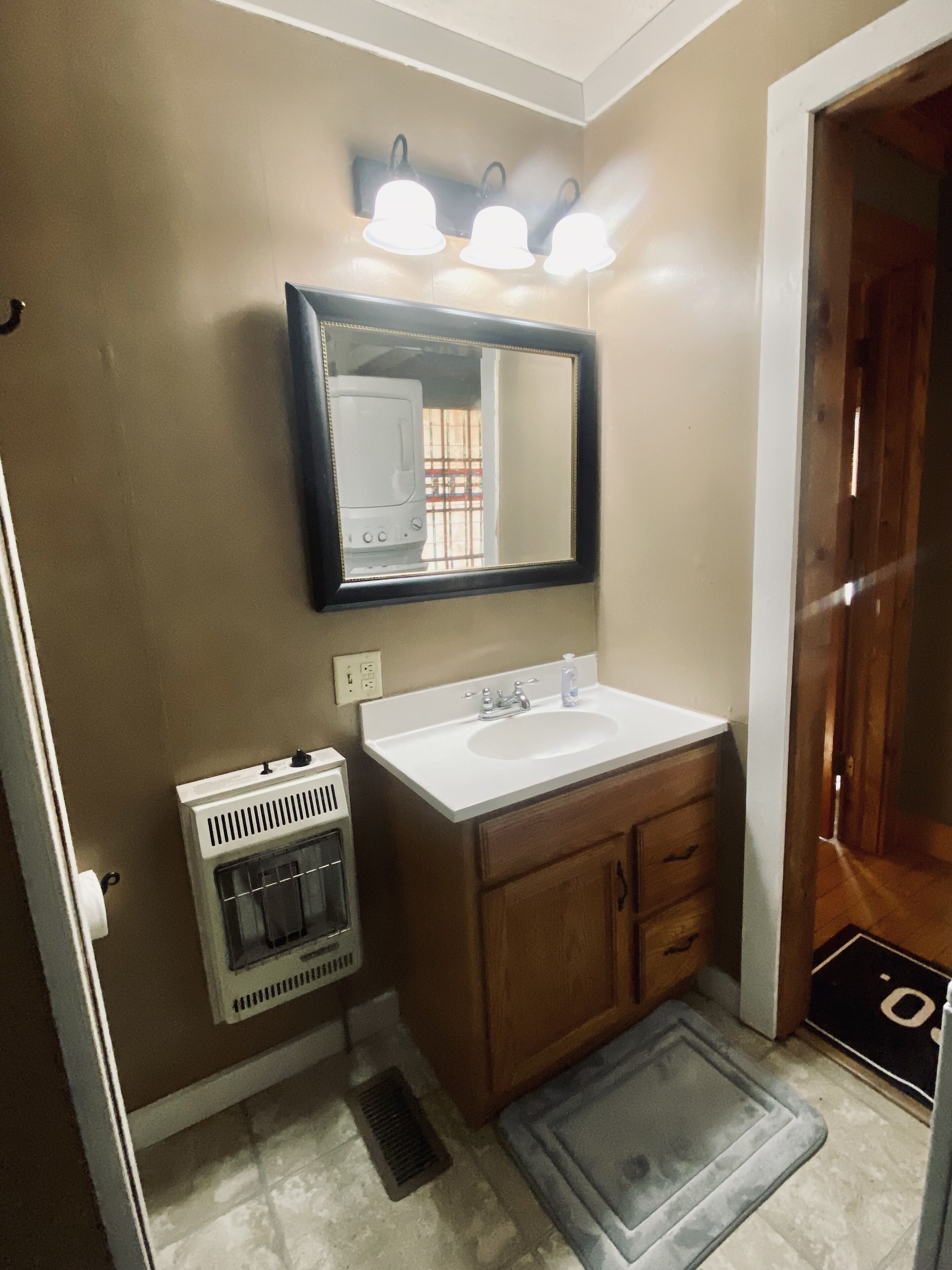 A bathroom with a white sink, wooden cabinets, a mirror, and a heater.
