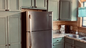 A kitchen with wooden cabinets, a stainless steel refrigerator, a coffee maker, and a sink. - 🌟Cozy Mountain Cabin with New Hot Tub🌟 (Mentone)