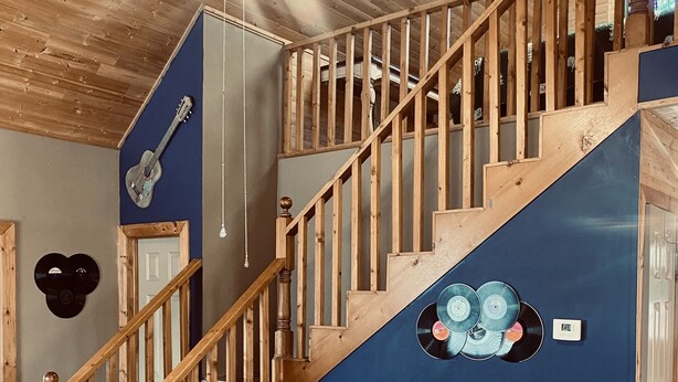 A wooden staircase with a blue wall, a black leather sofa, and a ceiling fan. - 🌟Cozy Mountain Cabin with New Hot Tub🌟 (Mentone)