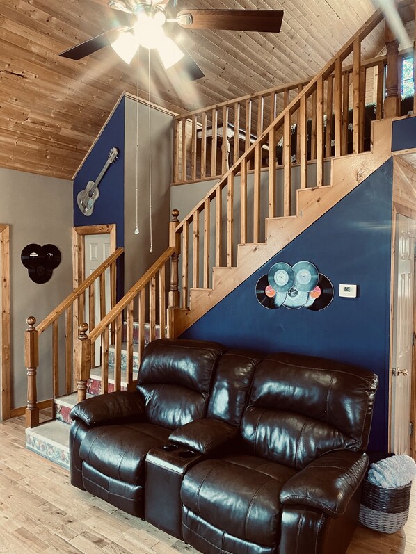 Eine Holztreppe mit blauer Wand, einem schwarzen Ledersofa und einem Deckenventilator.