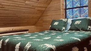 A wooden cabin bedroom with a bed, pillows, and a stained glass window. - 🌟Cozy Mountain Cabin with New Hot Tub🌟 (Mentone)