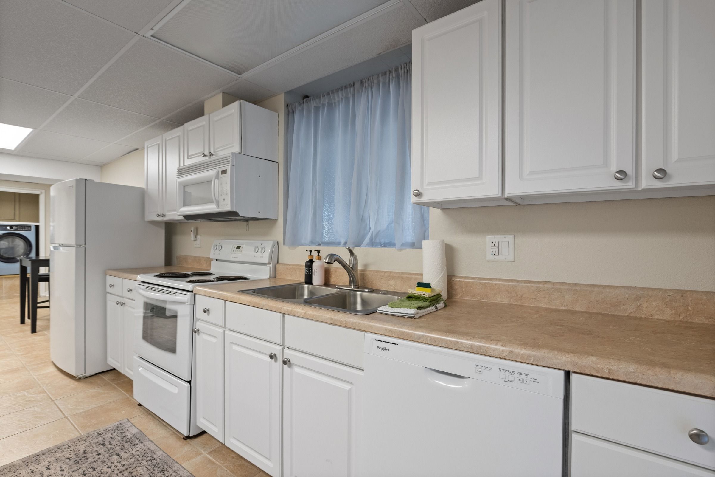 Cocina compacta con muebles blancos, horno microondas integrado, estufa y lavavajillas.