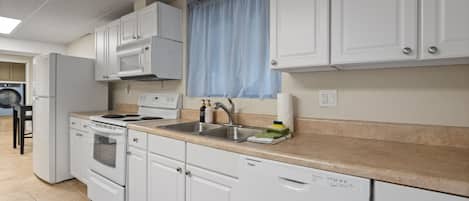 Cocina compacta con muebles blancos, horno microondas integrado, estufa y lavavajillas.