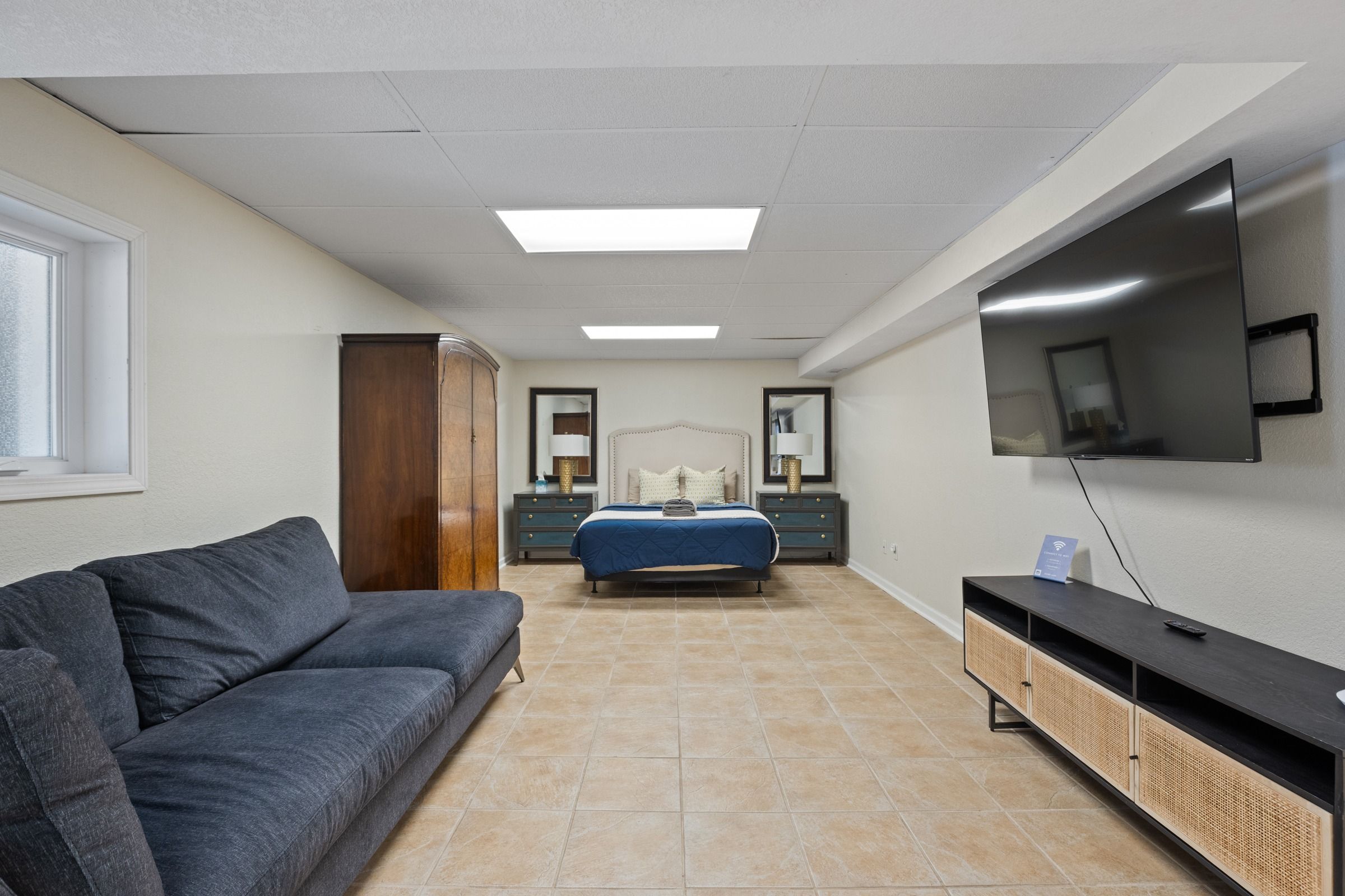 Une chambre à coucher avec un lit, un téléviseur fixé au mur, un canapé et un meuble.