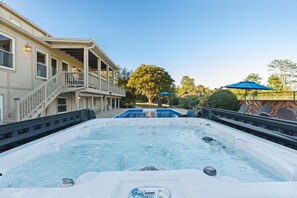 A hot tub with a pool in the background, a covered deck area, and a building with a balcony.