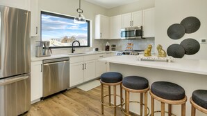 Una cocina moderna con electrodomésticos de acero inoxidable, armarios blancos y un ventanal amplio.