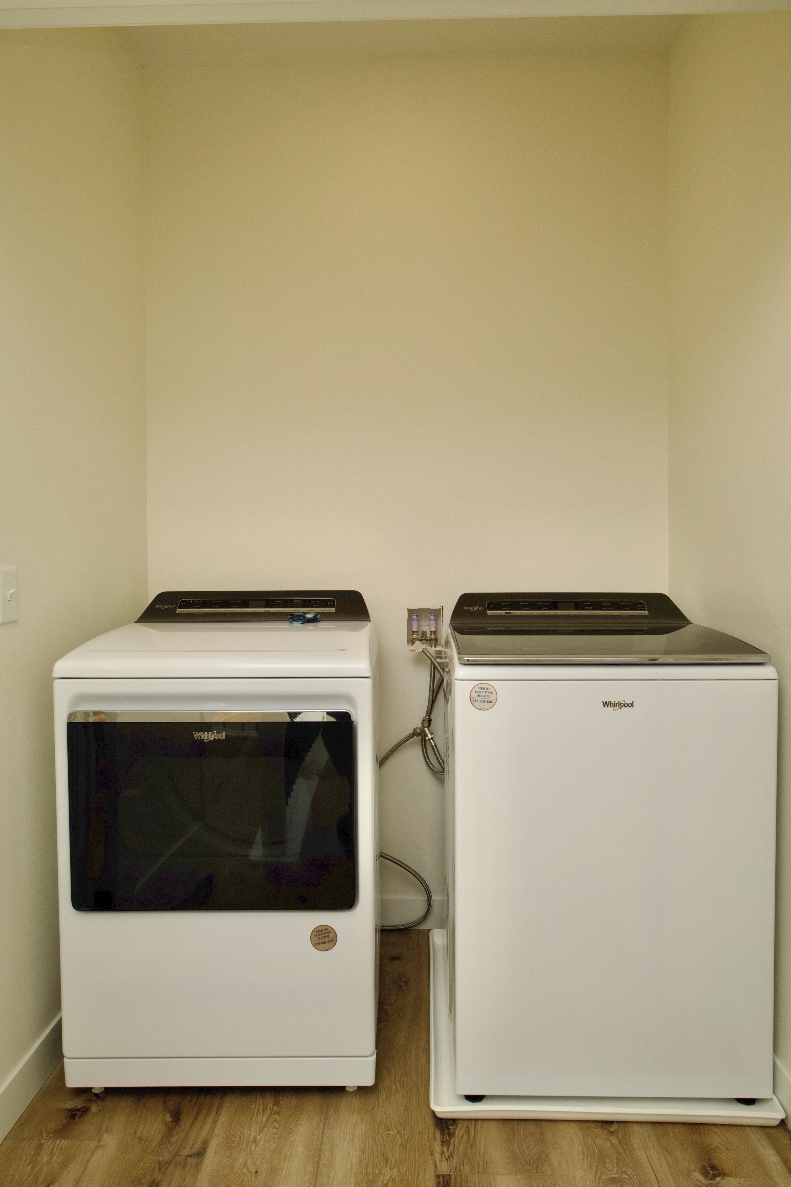 Two white appliances, one with a glass door and the other with a solid door, placed against a wall with a wooden floor.