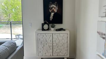 Una sala moderna con un sofá gris, un mueble blanco con diseño de ladrillo, un cuadro con la imagen de un perro y un reloj.