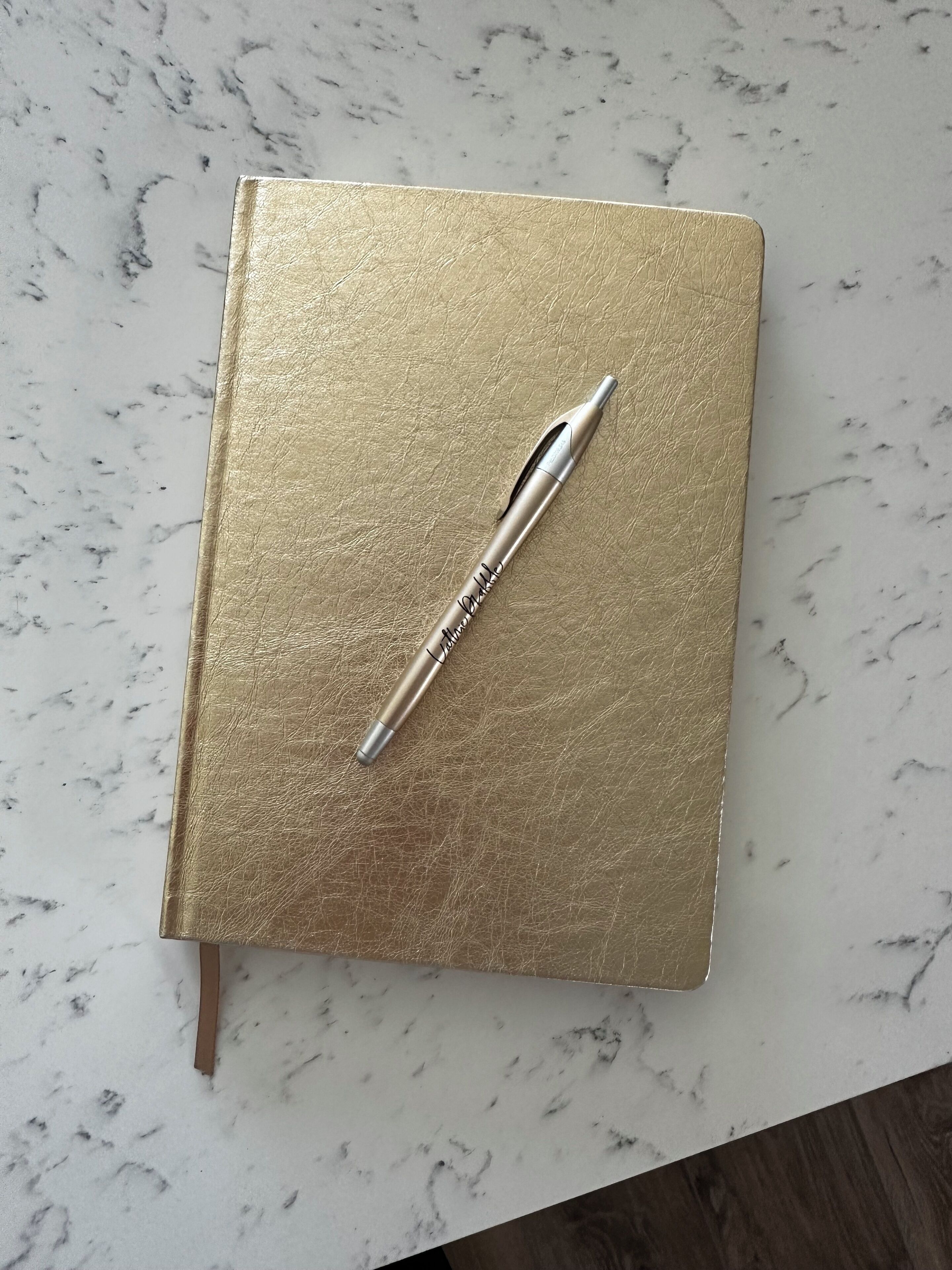 Una libreta dorada con un bolígrafo sobre una superficie de mármol.