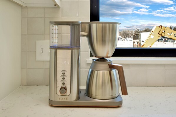 A coffee maker with a digital display and a large stainless steel pot on a kitchen counter.