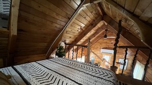 A wooden interior with a high ceiling, a patterned rug, and a potted plant.