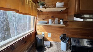 A compact kitchen with wooden cabinets, a stainless steel stove, and a window with a view of trees.