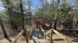 A wooden boardwalk leading to a cabin with a red roof, surrounded by trees.
