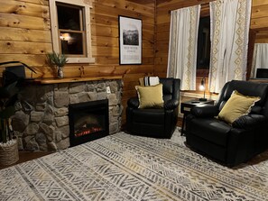 Interior acogedor de una cabaña con chimenea de piedra, dos sillones de cuero, un tapete estampado y un cuadro enmarcado de un cañón.