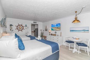 A room with two beds, a desk, a chair, a dining table, and nautical-themed decor.
