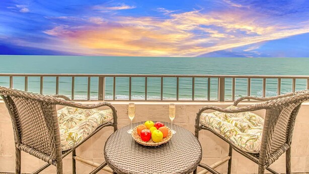 Un balcone con sedie in vimini e un tavolo, affacciato sul mare con vista sul tramonto.