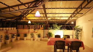 A covered outdoor dining area with a table and chairs, surrounded by potted plants and a hammock. - The WAVES by the Beach Inn (Kochi)
