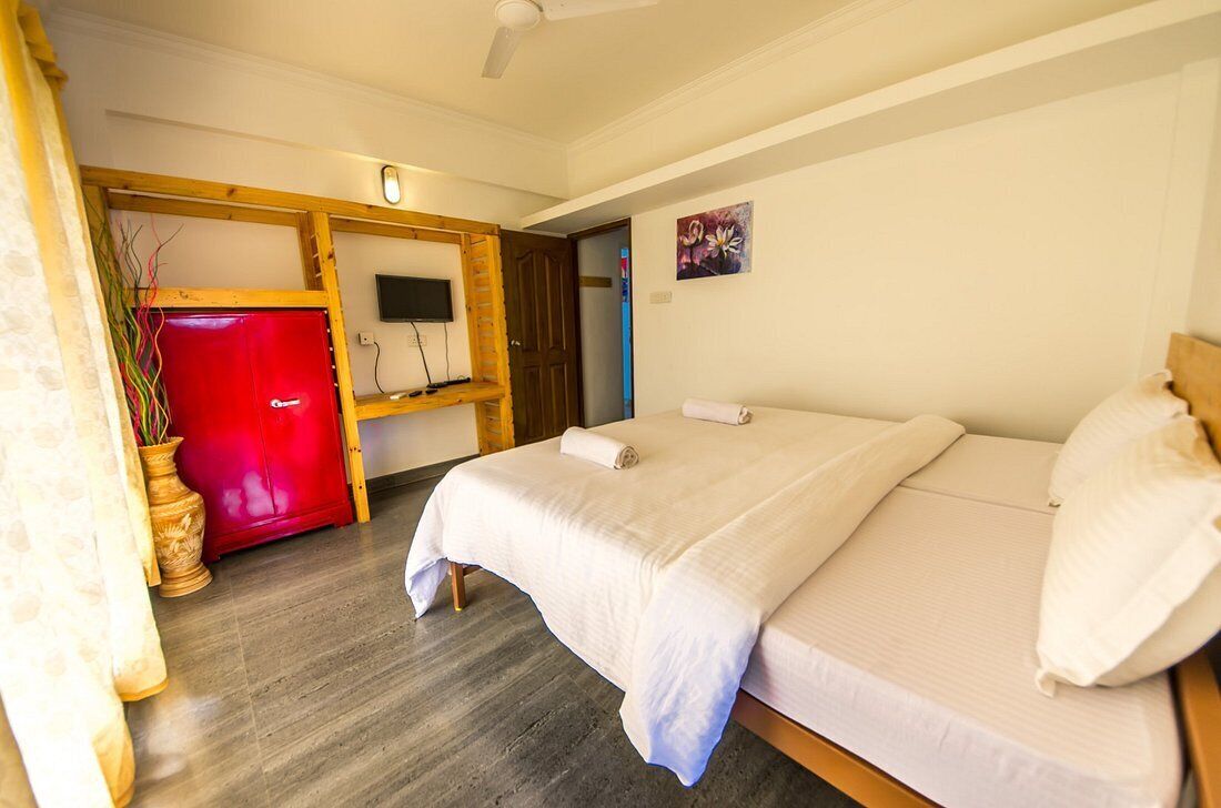 A hotel room with a bed, a TV, a red cabinet, and a door leading to another room.