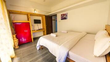 A hotel room with a bed, a TV, a red cabinet, and a door leading to another room.