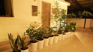A room with a tiled floor, a white sink, a wooden door, and several potted plants arranged in a row. - The WAVES by the Beach Inn (Kochi)