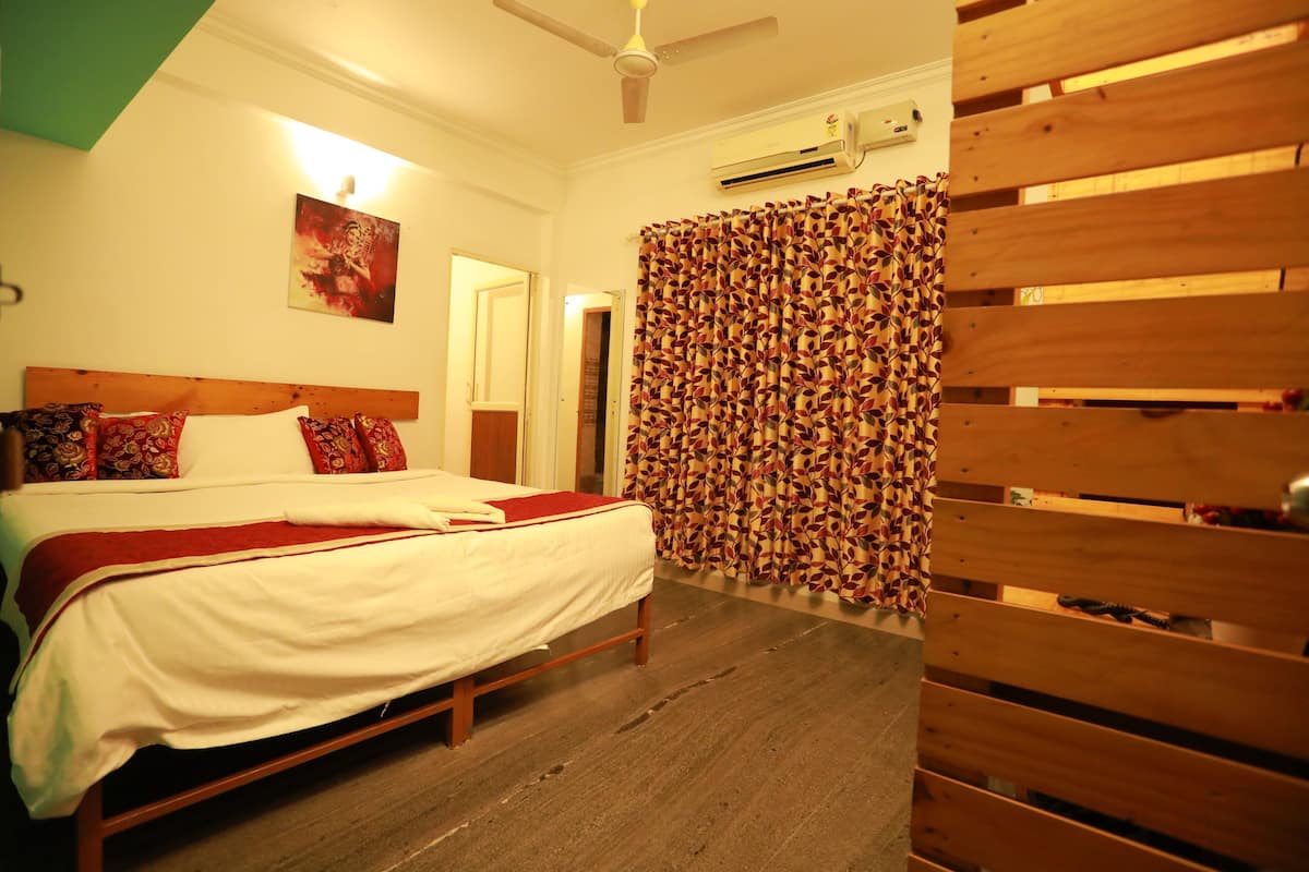 Quarto com cama, cabeceira de madeira, cortinas estampadas e um aparelho de ar condicionado.