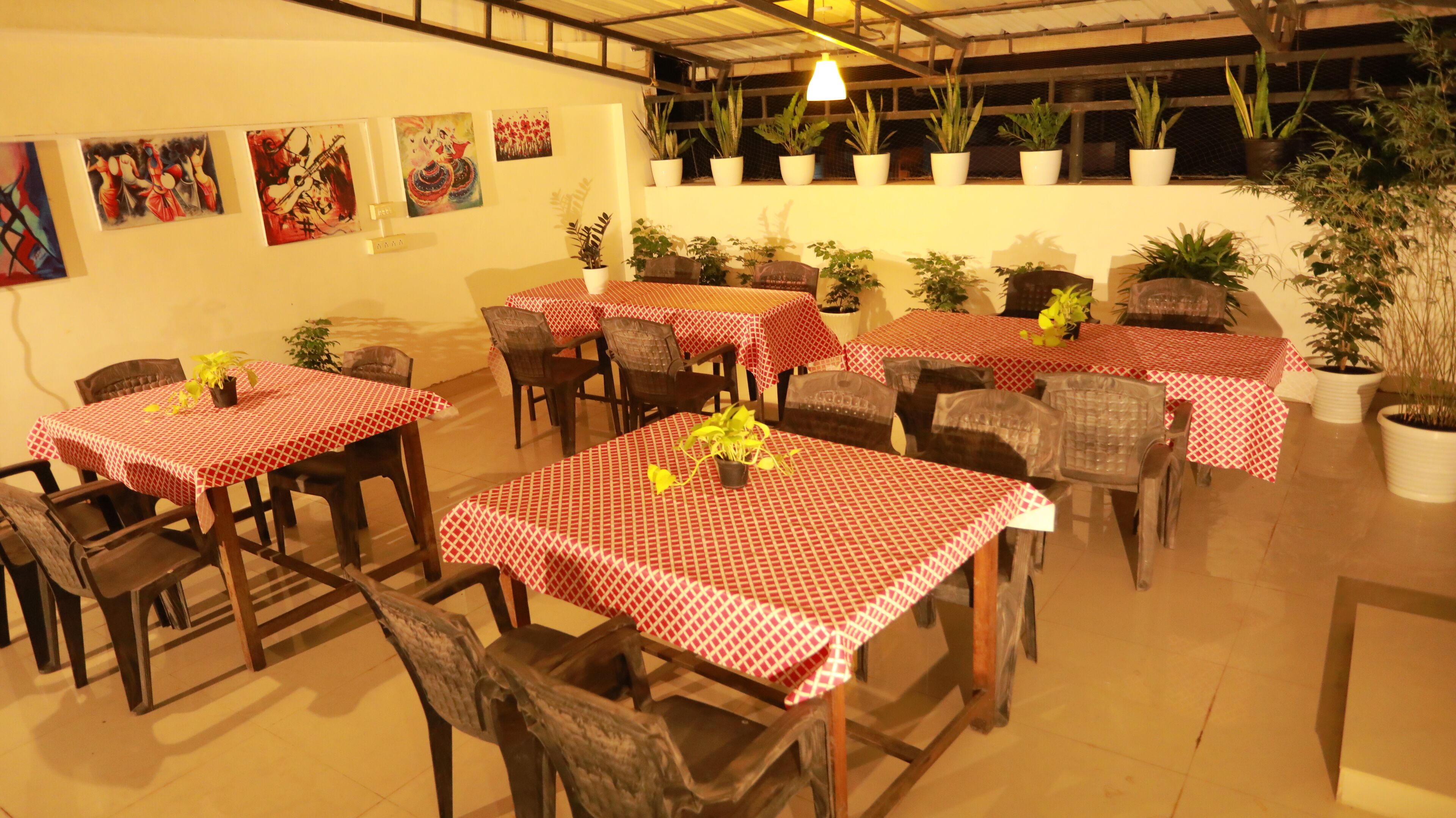A restaurant with multiple tables covered in red and white checkered tablecloths, surrounded by potted plants and chairs.