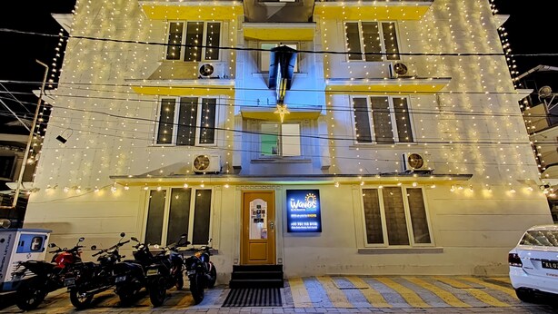 A building with a sign reading "Waves" and a contact number. There are motorcycles parked in front. - The WAVES by the Beach Inn (Kochi)