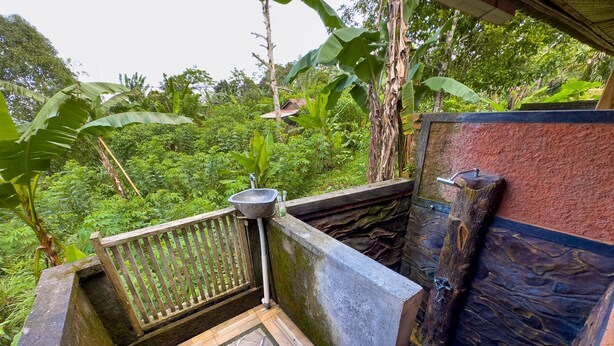 A stone sink with a wooden bench, surrounded by lush greenery and a stone wall.
