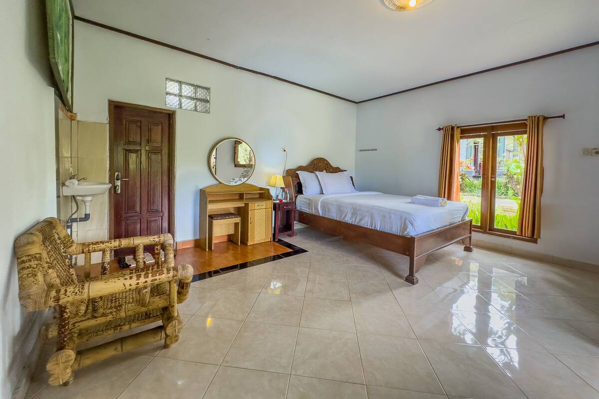 Ein Schlafzimmer mit Bett, Holztisch, Stuhl und einem Badezimmer mit Waschbecken und Spiegel.